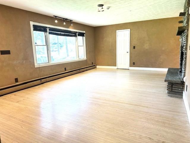 unfurnished living room with baseboards, wood finished floors, rail lighting, and a baseboard radiator