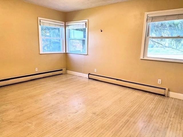 spare room featuring baseboard heating, baseboards, a baseboard heating unit, and wood finished floors