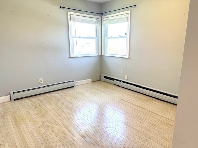 unfurnished room featuring baseboards, baseboard heating, and wood finished floors
