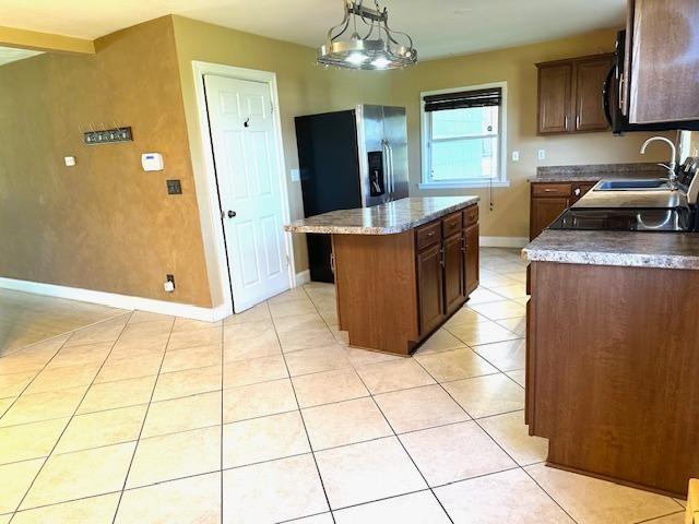 kitchen featuring dark brown cabinetry, a center island, a sink, baseboards, and light tile patterned floors