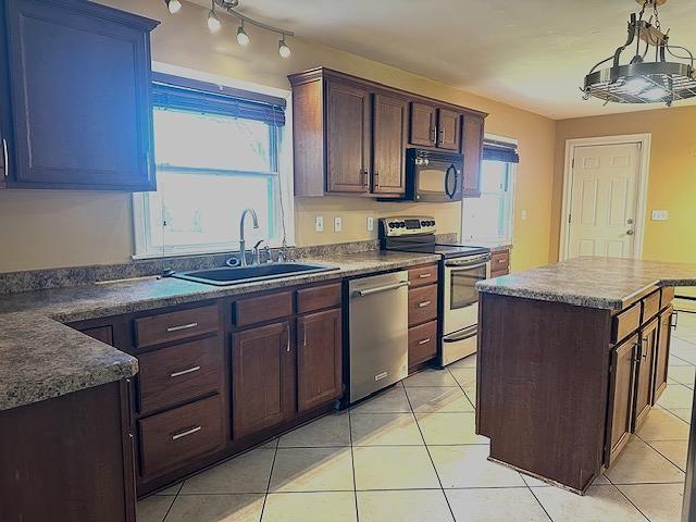 kitchen featuring a kitchen island, light tile patterned floors, appliances with stainless steel finishes, and a sink