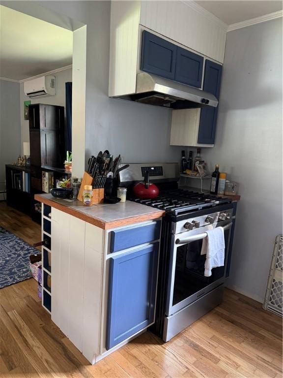 kitchen featuring crown molding, a wall mounted air conditioner, stainless steel gas stove, light wood finished floors, and under cabinet range hood