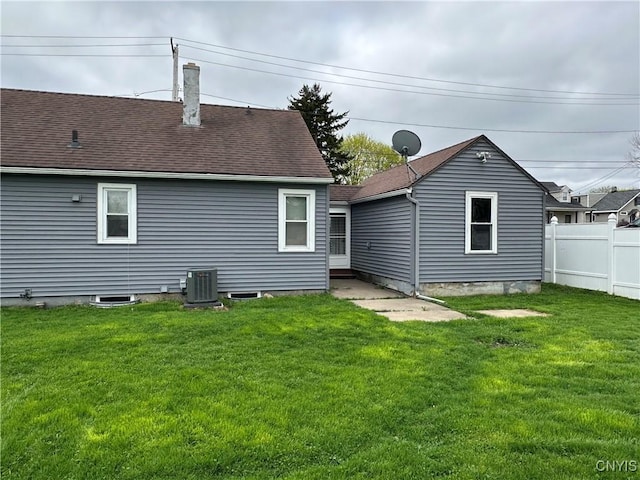 rear view of property featuring fence, roof with shingles, a chimney, central air condition unit, and a yard
