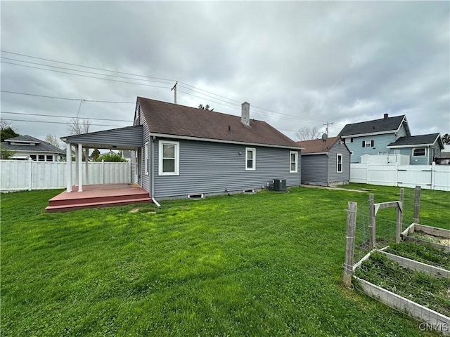 back of house featuring a lawn, central AC unit, fence, and a vegetable garden