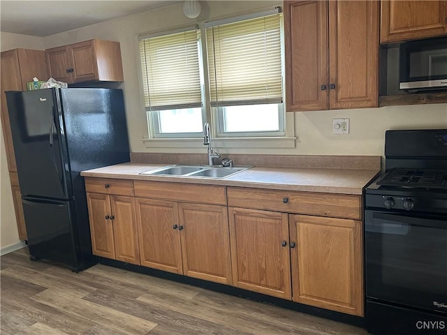 kitchen featuring light wood-style floors, a sink, brown cabinets, and black appliances