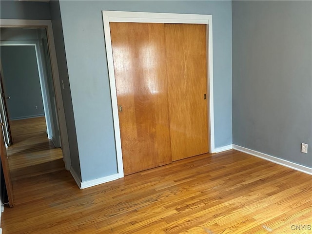 unfurnished bedroom featuring a closet, light wood-style flooring, and baseboards