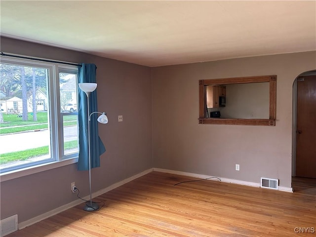 spare room featuring arched walkways, baseboards, light wood-type flooring, and visible vents