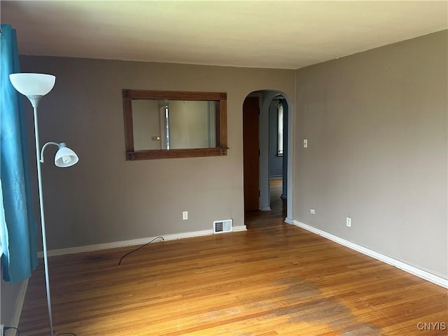 unfurnished room with arched walkways, baseboards, visible vents, and light wood-style flooring