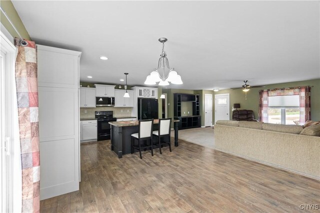 kitchen with a kitchen breakfast bar, white cabinetry, open floor plan, a kitchen island, and black appliances