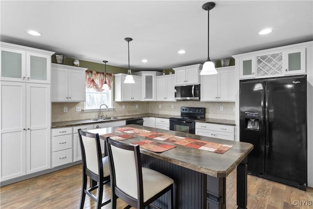 kitchen featuring white cabinetry, dark countertops, a sink, and black appliances