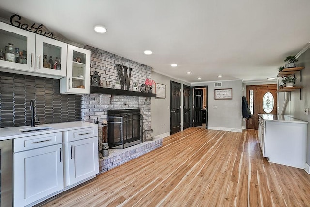 unfurnished living room with crown molding, a sink, light wood finished floors, and a fireplace