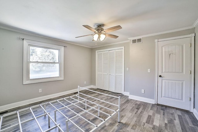 unfurnished bedroom featuring visible vents, wood finished floors, baseboards, a closet, and ornamental molding