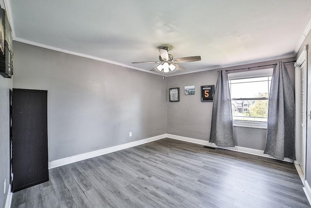 empty room featuring visible vents, ornamental molding, wood finished floors, baseboards, and a ceiling fan