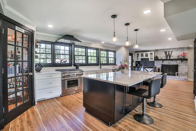 kitchen with crown molding, stainless steel range, a brick fireplace, a breakfast bar area, and white cabinetry