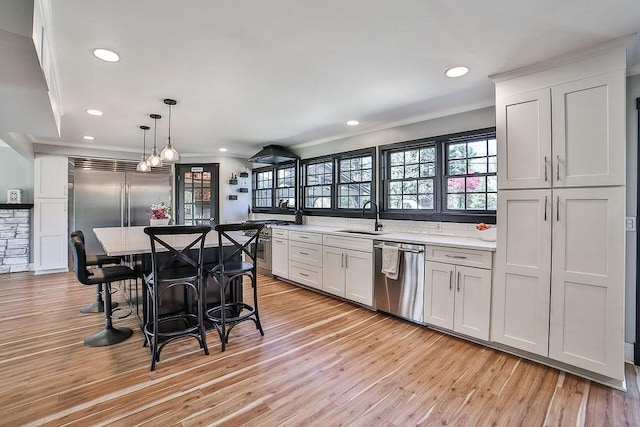 kitchen featuring crown molding, appliances with stainless steel finishes, a sink, light wood-style floors, and light countertops