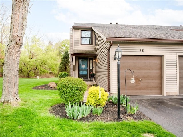 view of front of property featuring an attached garage, a shingled roof, a front lawn, and aphalt driveway