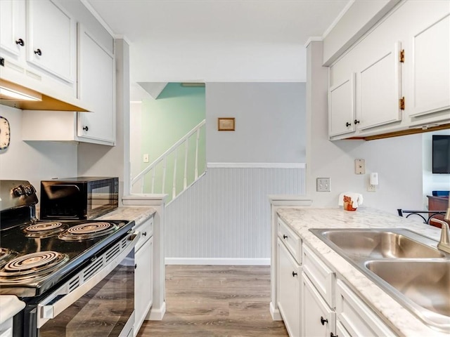 kitchen featuring a sink, light wood finished floors, white cabinetry, under cabinet range hood, and black appliances