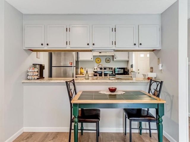 kitchen featuring appliances with stainless steel finishes, a sink, baseboards, light wood finished floors, and under cabinet range hood