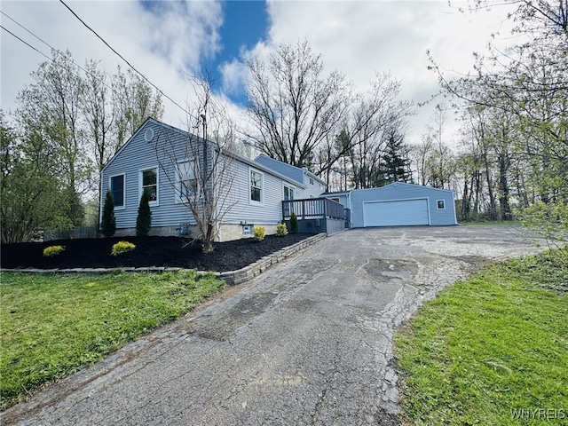 view of home's exterior with aphalt driveway, a detached garage, a deck, an outbuilding, and a lawn