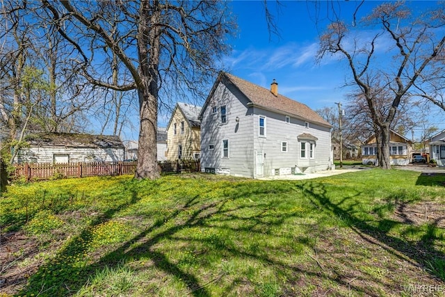 view of side of property featuring fence, a yard, and a chimney