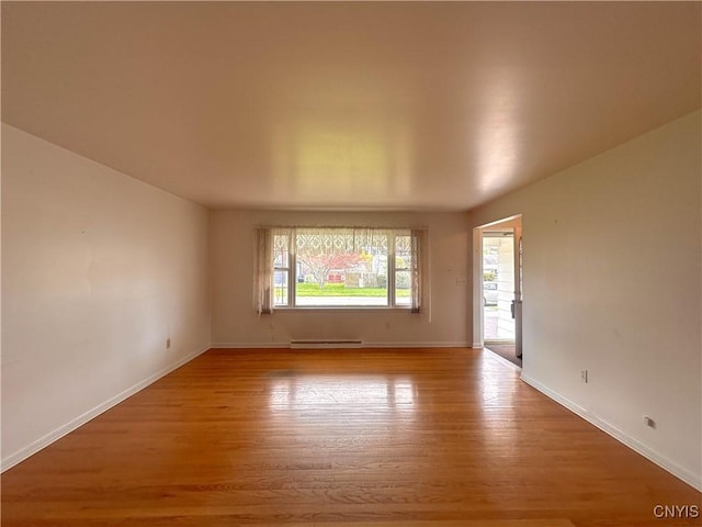 empty room featuring baseboards, a baseboard radiator, and wood finished floors