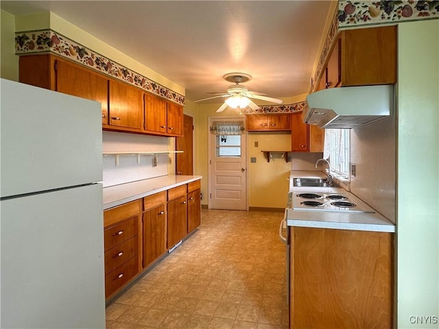 kitchen featuring a sink, light countertops, freestanding refrigerator, light floors, and under cabinet range hood