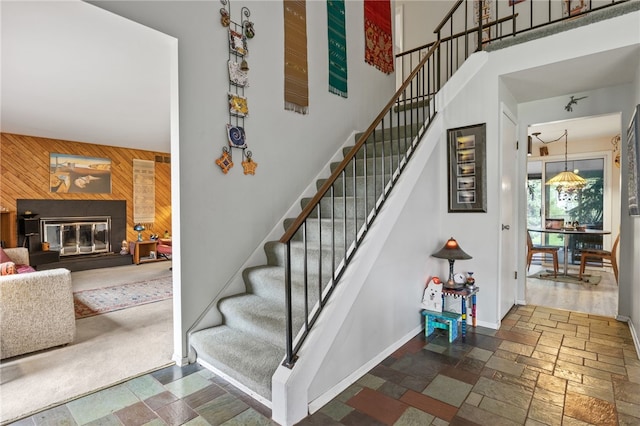 stairs with wood walls, a glass covered fireplace, baseboards, a towering ceiling, and stone tile flooring