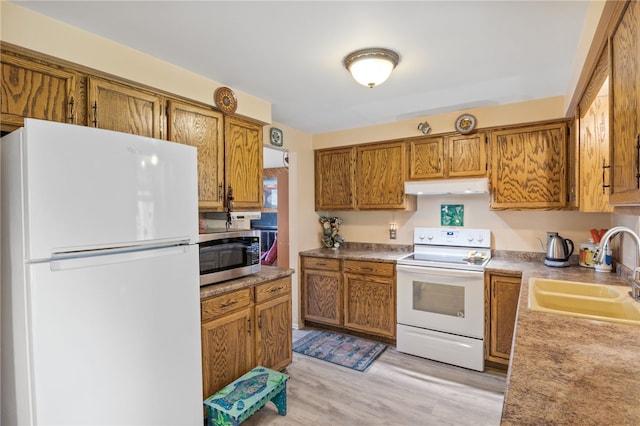 kitchen with brown cabinetry, white appliances, light wood-style floors, under cabinet range hood, and a sink