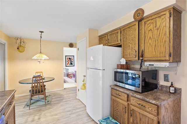 kitchen featuring dark countertops, light wood-style floors, freestanding refrigerator, stainless steel microwave, and pendant lighting