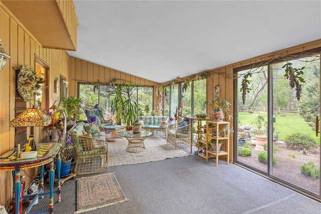 unfurnished sunroom featuring carpet floors, wood walls, an outdoor living space, and vaulted ceiling