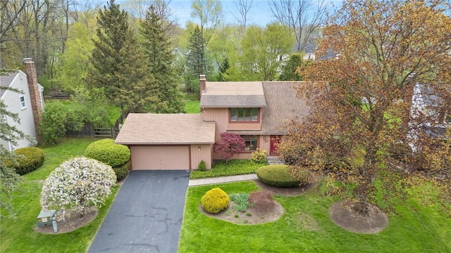 view of front facade featuring a garage, a front lawn, roof with shingles, a chimney, and driveway