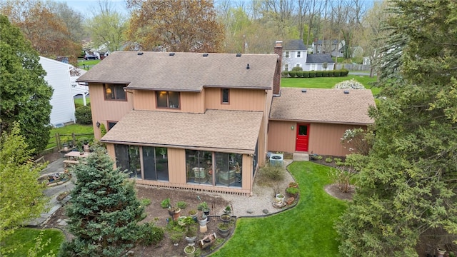 back of property with roof with shingles, fence, a sunroom, a chimney, and a lawn