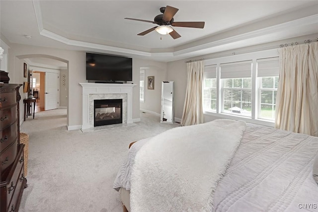 carpeted bedroom featuring a ceiling fan, a high end fireplace, arched walkways, a raised ceiling, and baseboards