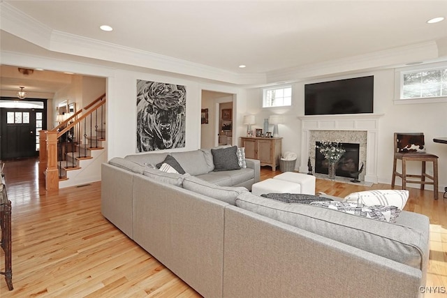 living room featuring crown molding, a fireplace, stairs, light wood finished floors, and recessed lighting
