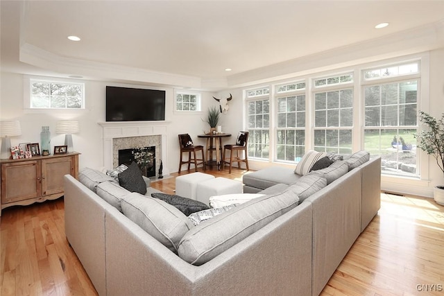 living room with crown molding, recessed lighting, a high end fireplace, a tray ceiling, and light wood-style flooring