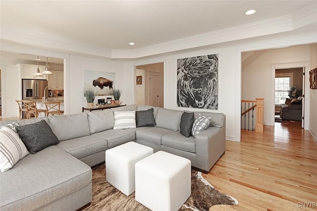 living room featuring crown molding, baseboards, a tray ceiling, recessed lighting, and light wood-style flooring