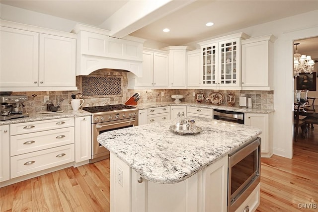 kitchen with light wood finished floors, appliances with stainless steel finishes, white cabinetry, and glass insert cabinets