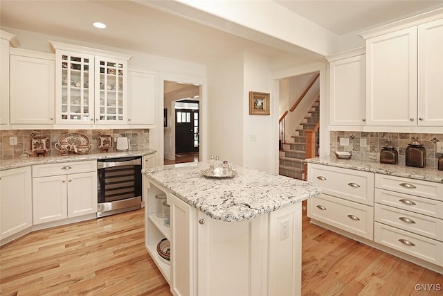 kitchen featuring beverage cooler, decorative backsplash, light wood-style floors, and white cabinetry