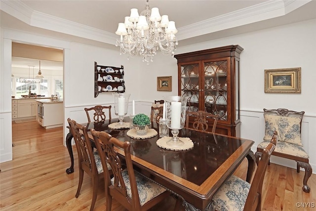 dining room with crown molding, a notable chandelier, light wood-style flooring, and a decorative wall