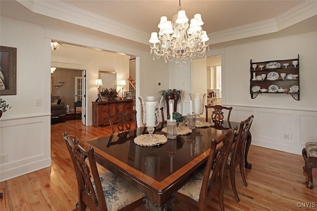 dining area with ornamental molding, light wood finished floors, a decorative wall, and a raised ceiling