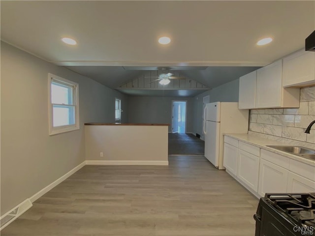 kitchen featuring a ceiling fan, freestanding refrigerator, baseboards, white cabinets, and a sink