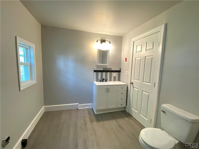 bathroom featuring toilet, baseboards, wood finished floors, and vanity