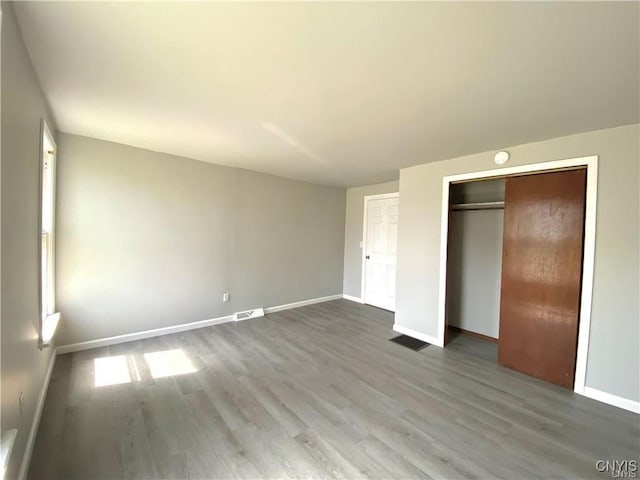 unfurnished bedroom featuring baseboards, visible vents, wood finished floors, and a closet