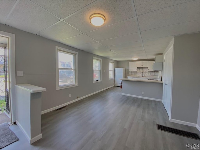 unfurnished living room with visible vents, wood finished floors, baseboards, a drop ceiling, and a sink