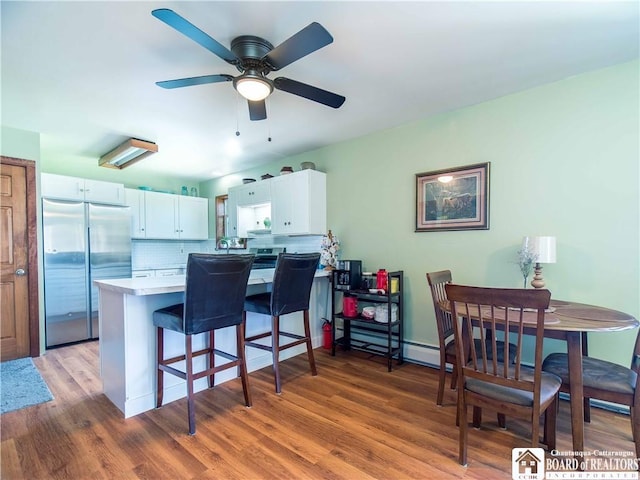 5585 Eke Rd, Harmony, NY 14710 - kitchen with stainless steel refrigerator, a peninsula, wood finished floors, a breakfast bar, and white cabinetry