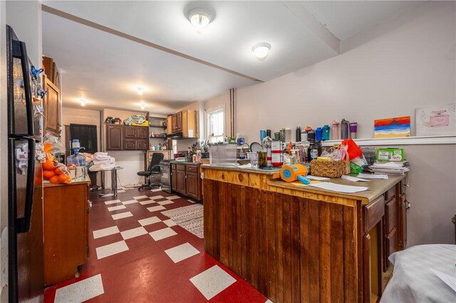 kitchen featuring open shelves, stainless steel stove, light countertops, freestanding refrigerator, and dark floors