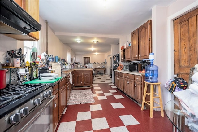 kitchen featuring stainless steel range with gas stovetop, brown cabinets, ventilation hood, a peninsula, and dark floors