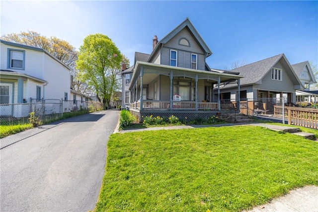 victorian-style house featuring fence, covered porch, a front yard, a chimney, and a residential view
