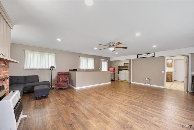 living room featuring a brick fireplace, a ceiling fan, recessed lighting, heating unit, and light wood-type flooring