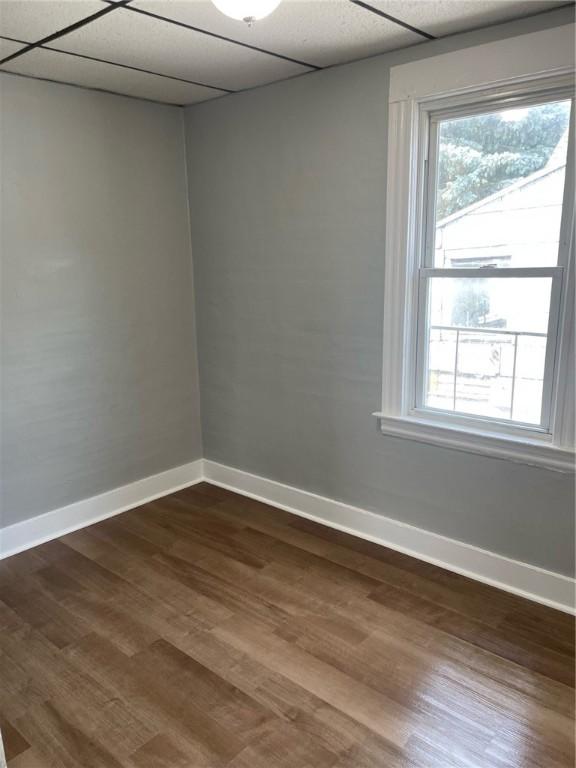 unfurnished room featuring dark wood-style flooring, baseboards, a healthy amount of sunlight, and a paneled ceiling
